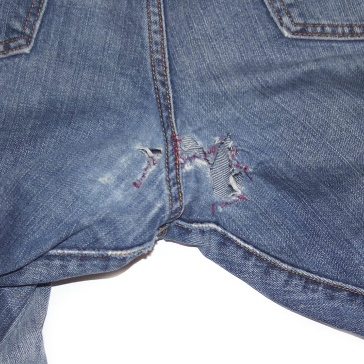 The before photo of jeans with Mom's DIY repairs of a crotch blowout displays red yarn used to hold the denim together.
