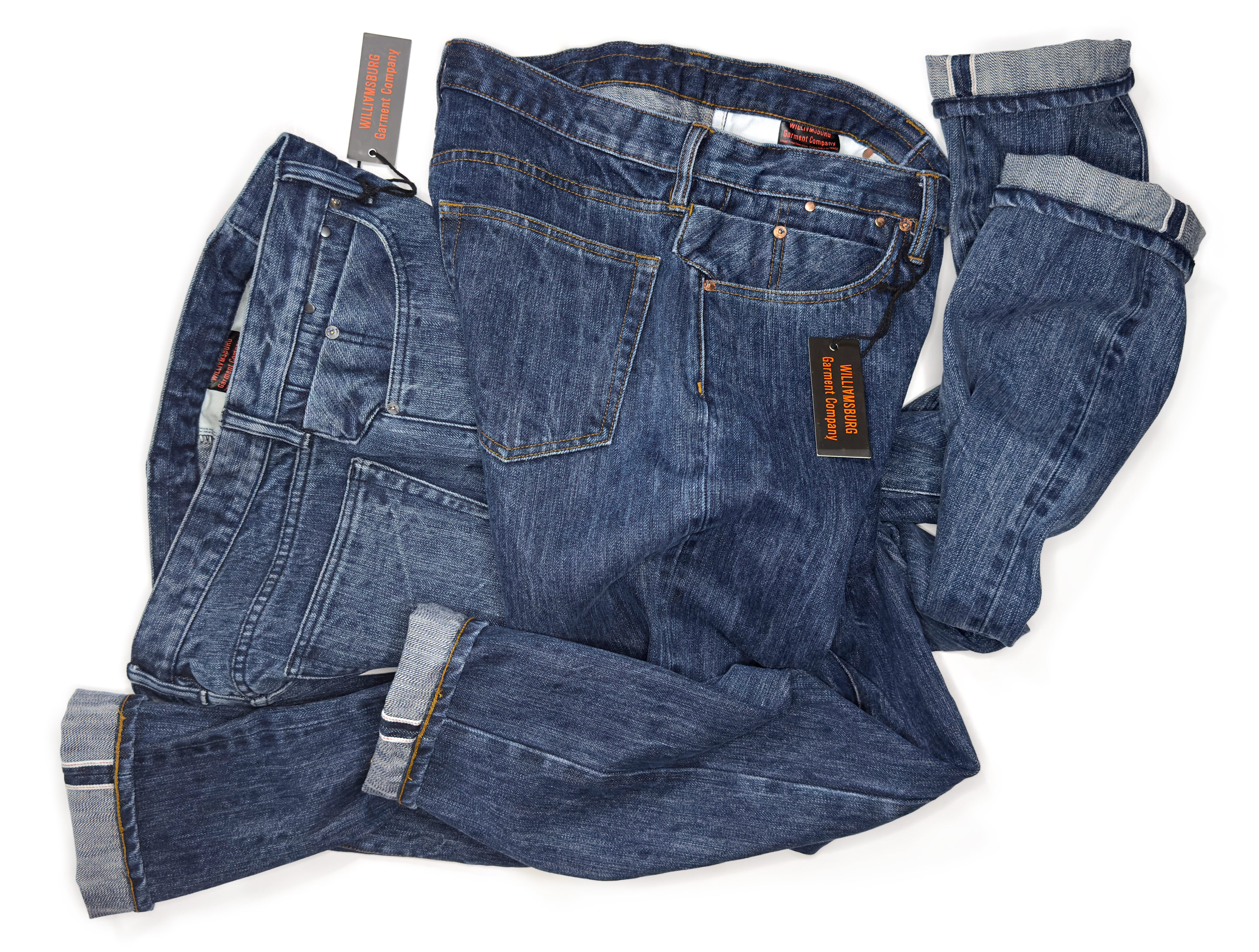 Two pair of Williamsburg Garment Company's light and dark washed custom blue jeans made in the USA twisting together on white background.