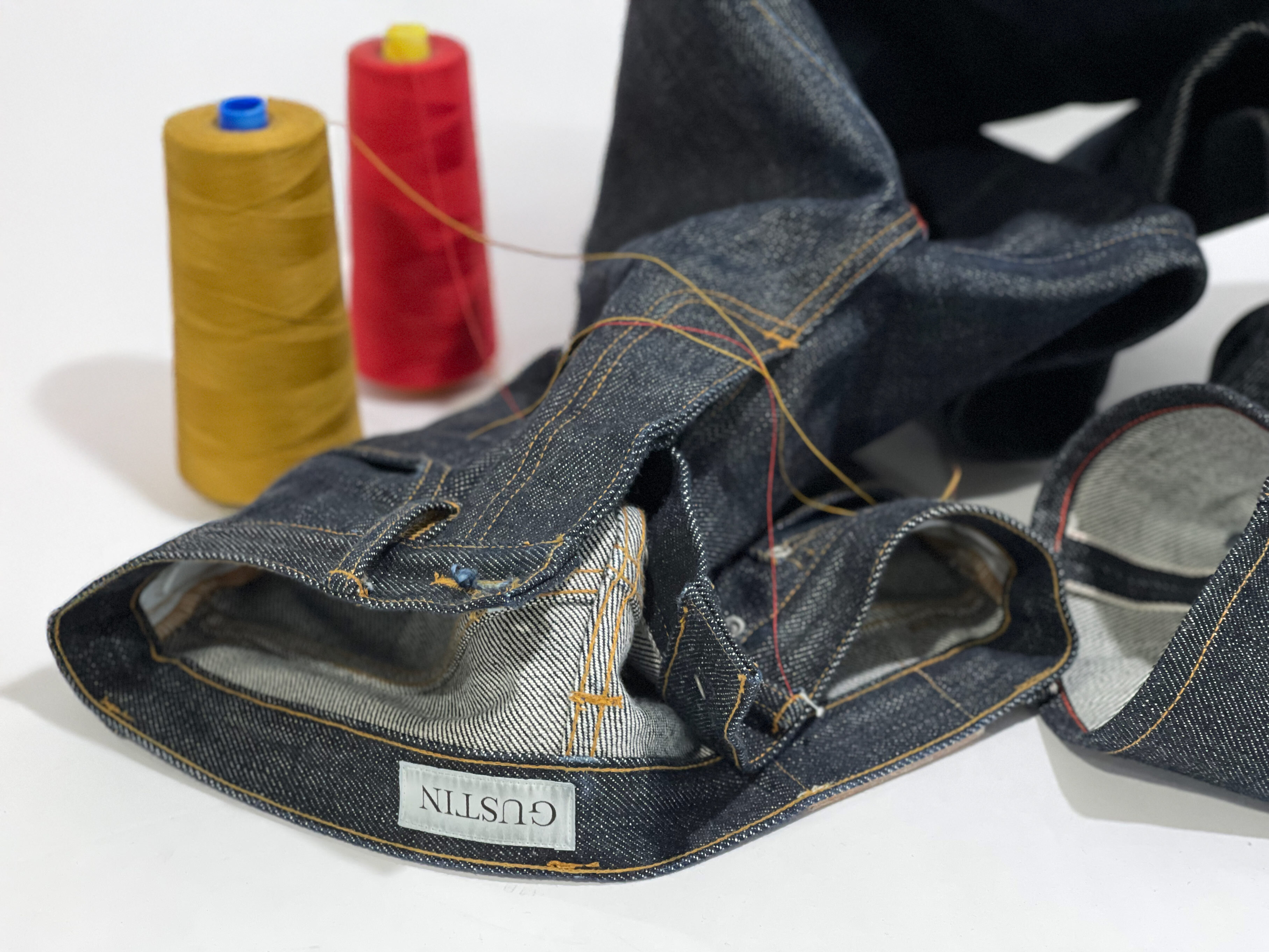 Gustin jeans prepared for chain stitch hemming by Williamsburg Garment Compnay, showing red bar tack and top stitching thread and chain stitch details