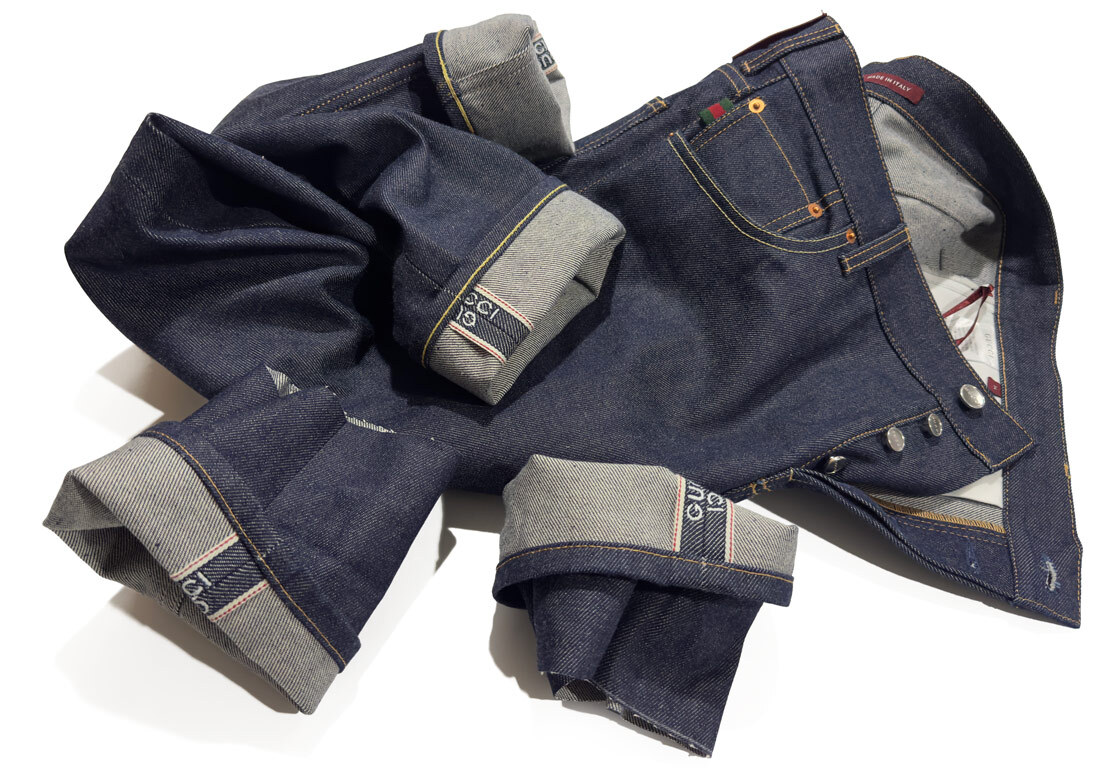 A pair of men's selvedge raw denim Gucci jeans with chain-stitch hemming alterations, showing the original lock-stitched hems in the foreground and the upgraded chain-stitched hems matching the pocket thread color.