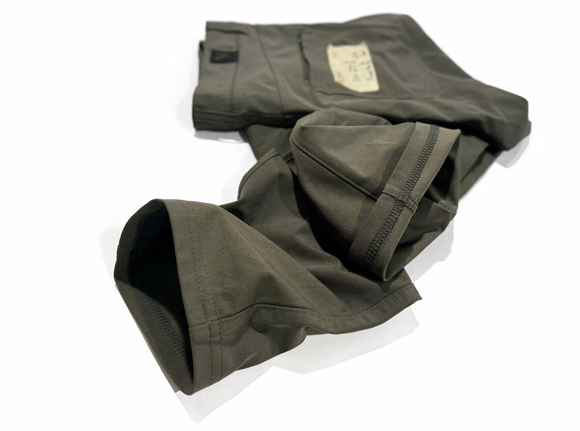 Close-up of dark oregano green professionally hemmed Vuori Meta pants using a coverstitch machine, showing the clean, flexible stitching on the inside of the pant leg.