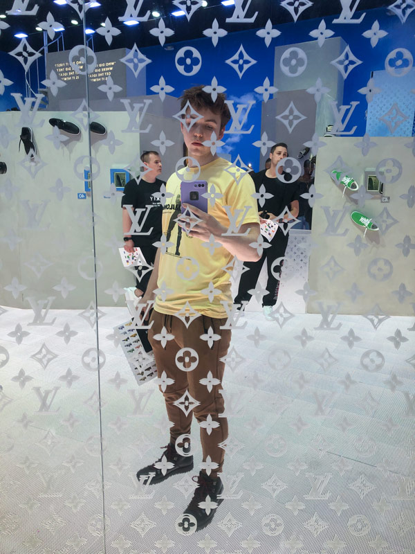 Josiah Rentschler selfie in front of mirror LV logo display wall.