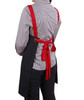 A black canvas bib apron with red straps tied at the back, worn by a person in a checkered shirt.