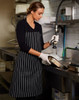 A black and white striped apron worn by a woman in a kitchen, featuring a logo, while washing dishes.
