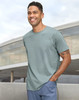 A man wearing a light green premium cotton short-sleeve T-shirt, standing outdoors with a modern building in the background.
