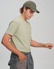 A light olive green men's premium cotton t-shirt worn with a matching cap and casual pants, featuring a logo.