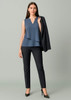 A woman wearing a sleeveless blue top and slim leg black pants, holding a black blazer.