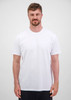 A man wearing a plain white short sleeve tee, standing against a neutral background. The tee features a logo.