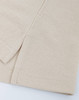 A close-up of a beige cotton/poly pique fabric, showcasing its texture and stitching details. It features a simple hemline.