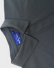 A grey polo shirt featuring a collar and a button, with a tag showing branding.