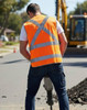 A safety vest in bright orange with reflective stripes, worn by a worker operating machinery on a construction site.