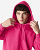 A bright pink hooded sweatshirt featuring a front pocket and drawstrings, worn by a model adjusting the hood.
