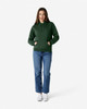 A woman wearing a green hooded sweatshirt with a kangaroo pocket, paired with blue jeans and white sneakers.