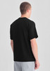 A black box tee viewed from the back, worn by a model in grey shorts. The shirt features a logo.