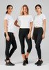 Three women in white t-shirts and black leggings, standing together against a grey background. The leggings have a logo.