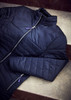A navy padded jacket laid flat, featuring a high collar and zip closure, with a logo visible on the zipper.