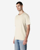 A beige Gildan Softstyle adult T-shirt features a relaxed fit and short sleeves, paired with light blue jeans.