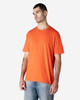 An orange Gildan Softstyle adult T-shirt displayed on a model wearing light blue jeans. The shirt features a logo.