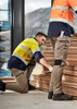 Two workers in high-visibility jackets and stretch cuffed pants, stacked wood planks in an industrial setting.