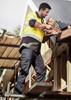A man in high-visibility clothing uses a nail gun while wearing navy lightweight drill cargo pants on a construction site.