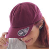 A maroon Dad Hat featuring a curved visor and a logo on the side, worn by a person with red hair.