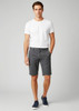 A model wearing grey dress shorts paired with a white t-shirt and navy shoes, featuring a branding logo.