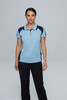 A woman stands wearing a light blue polo shirt with navy accents, paired with black pants. The shirt features a logo.