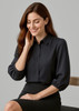 A woman in a black 3/4 sleeve blouse with a button front, sitting on a chair, smiling.
