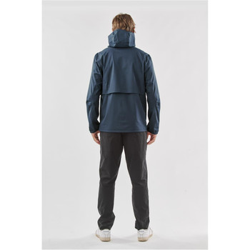 A man stands facing away, wearing a navy blue rain jacket with a hood, paired with dark trousers. A man stands facing away, wearing a navy blue rain jacket with a hood, paired with dark trousers.