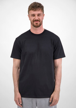 A man stands wearing a plain black short sleeve tee, with a neutral background. The tee features a logo.