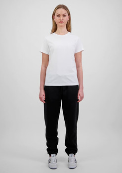 A woman in a white t-shirt and black track pants stands against a plain background. The pants have a branding logo.