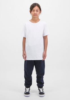 A child wears a white t-shirt and navy track pants, standing against a plain white background. The outfit features a logo.