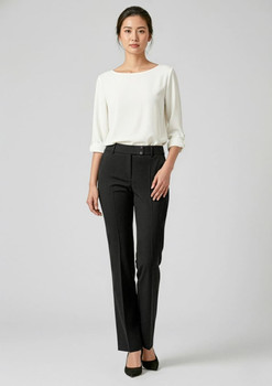 A woman stands in sleek black slacks paired with a light-coloured top and heels, showcasing a stylish look.