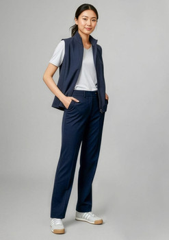 A woman stands in navy blue slacks paired with a white t-shirt and a navy vest, featuring a logo on the vest.