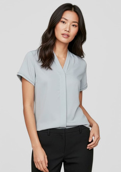 A light blue women's short sleeve button-up shirt displayed on a model, featuring a v-neckline and rolled sleeves.