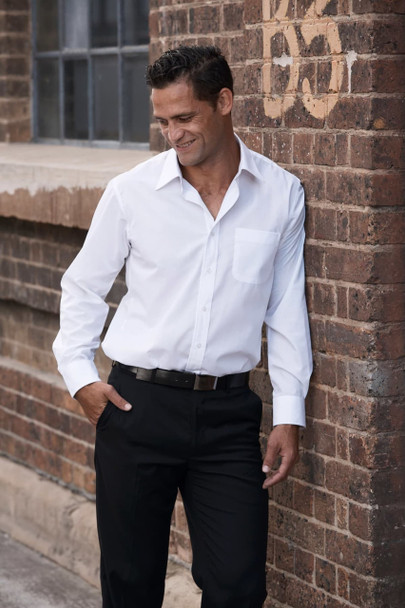 A long sleeve white button-up shirt on a man, paired with black trousers, against a brick wall background.