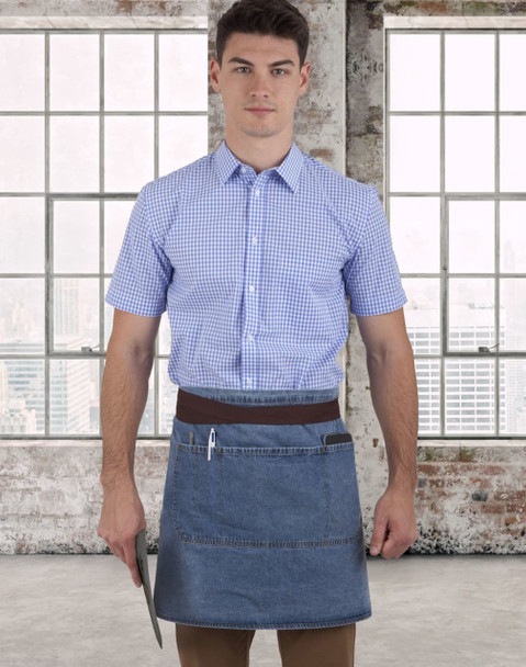 A denim half apron with a brown waistband, worn by a person in a blue checked shirt, against a city skyline backdrop.