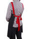 A black canvas bib apron with red straps tied at the back, worn by a person in a checkered shirt.