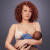 Confident woman wearing Elvie Curve on one side while breastfeeding baby on the other