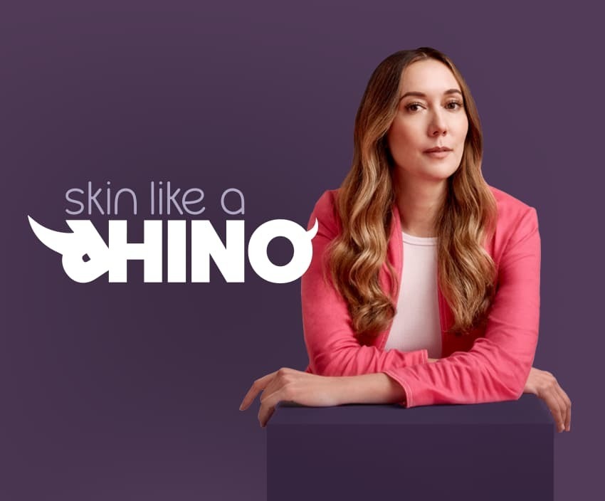 Elvie founder Tania Boler leaning forwards resting her elbows on a purple plinth, with the words Skin Like A Rhino next to her. The word Rhino has horns added to the R and the O