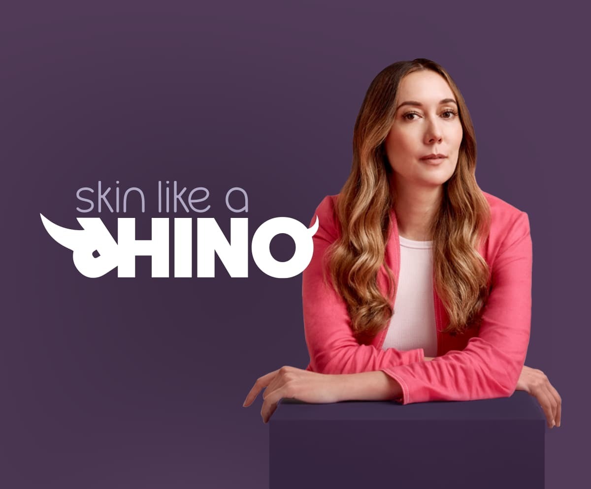 Elvie founder Tania Boler leaning forwards resting her elbows on a purple plinth, with the words Skin Like A Rhino next to her. The word Rhino has horns added to the R and the O