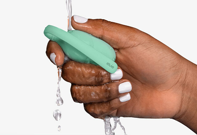 A close up of a woman's hand holding an Elvie Trainer under running water