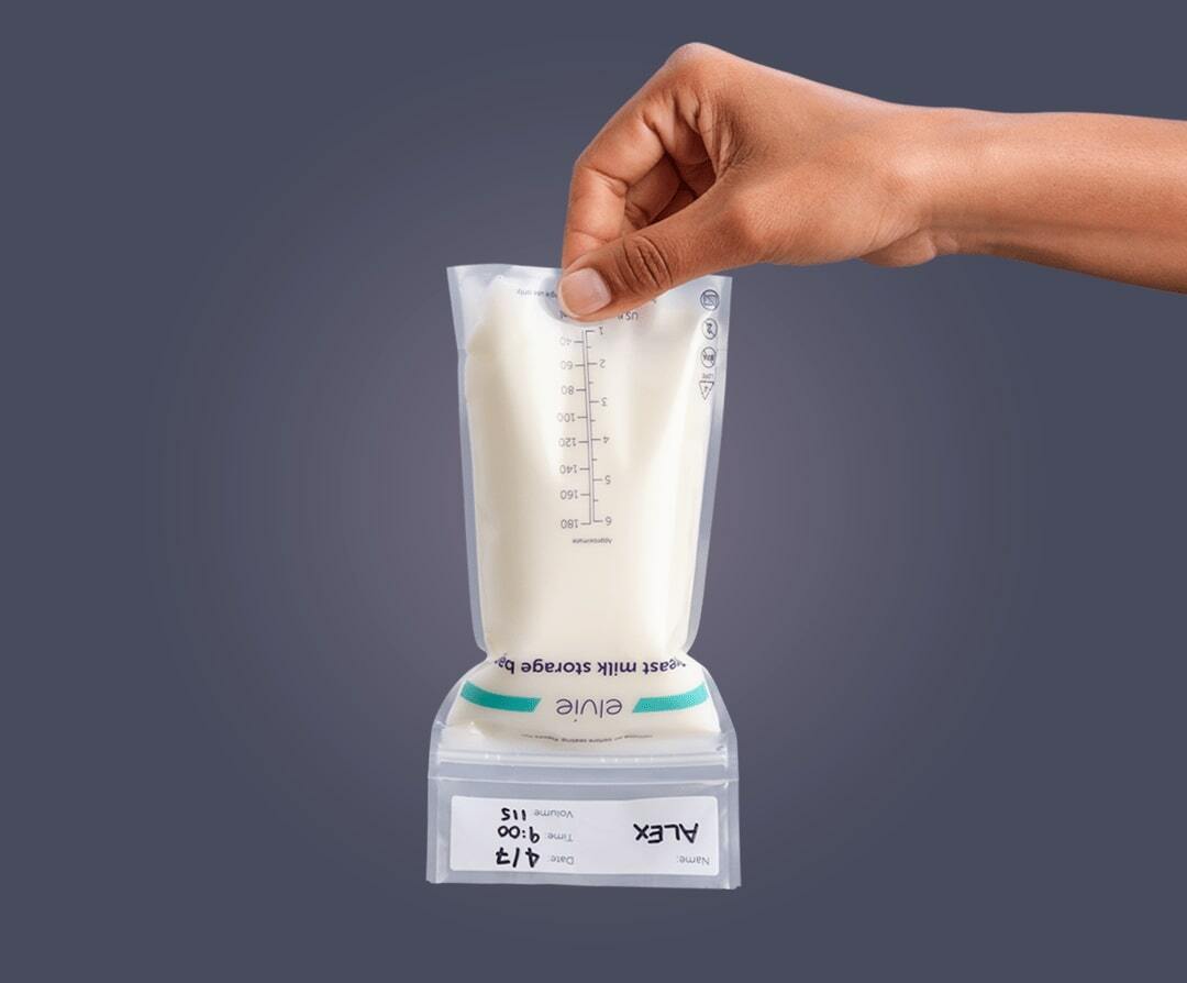 A woman's hand holding an Elvie milk bag upside down. It is full of milk and sealed