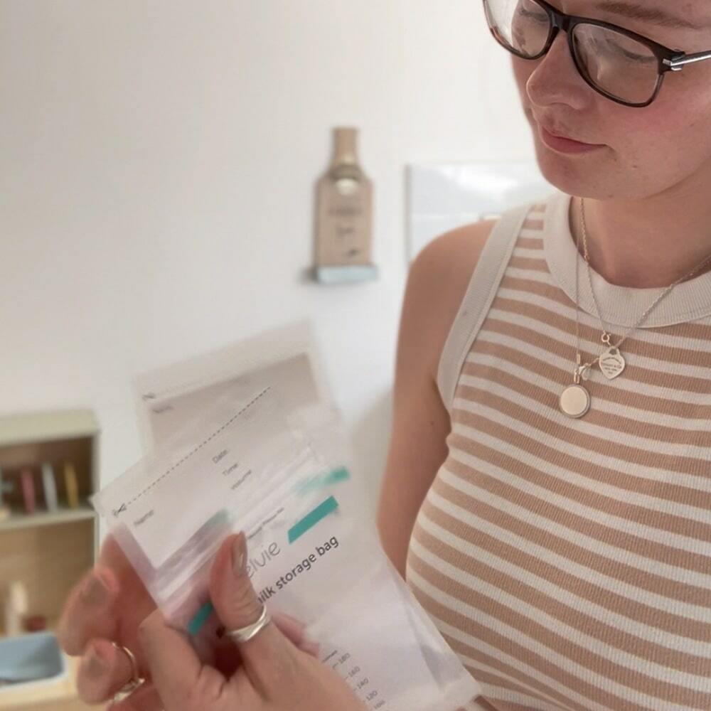 A woman holding two Elvie milk bags and looking down at them