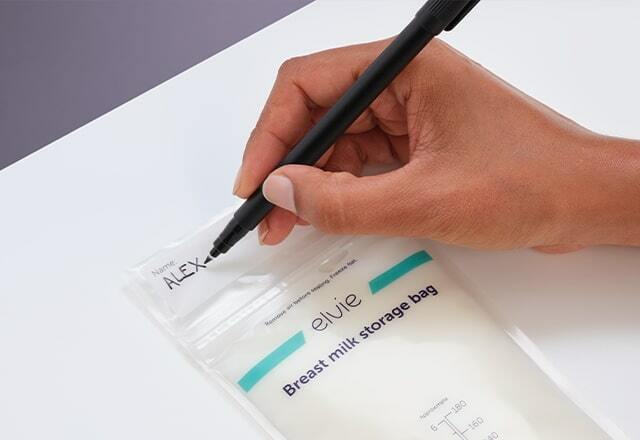 A woman's hand, writing the name Alex on the top of a full Elvie milk bag. There is a white box printed on the bag with dotted lines in it on which to write your information