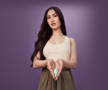 A woman holding an Elvie trainer between her thumb and finger. She is holding it up to the camera and her face is in the background out of focus