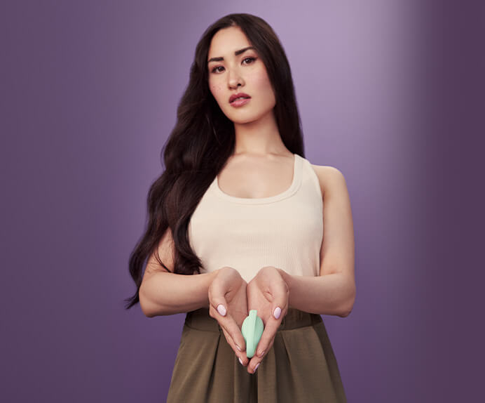 A woman holding an Elvie trainer between her thumb and finger. She is holding it up to the camera and her face is in the background out of focus