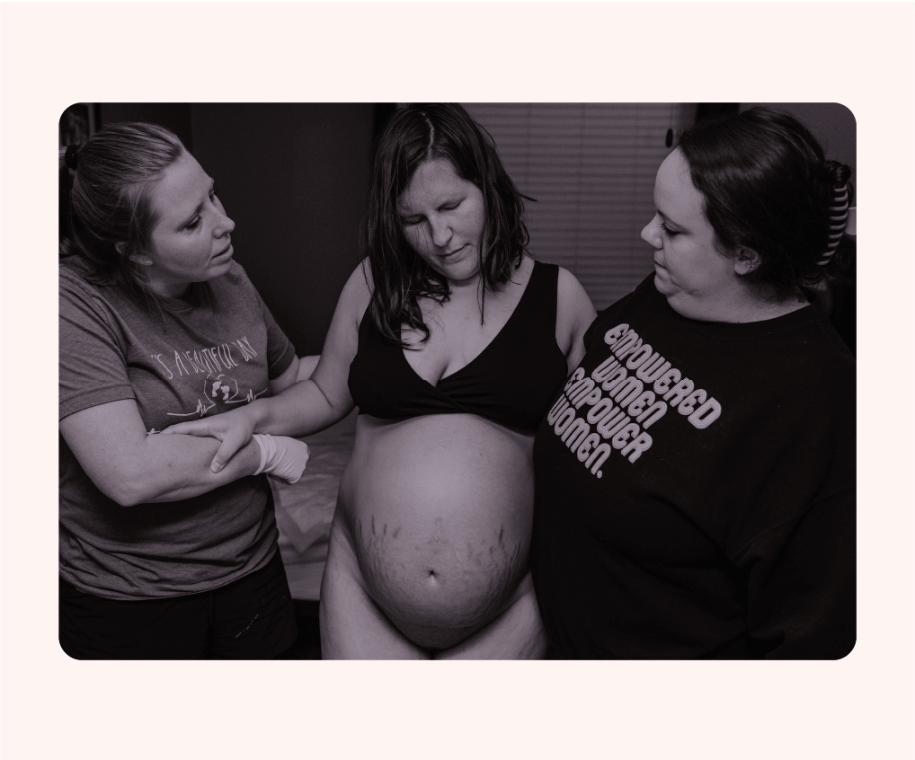 A pregnant woman in her underwear, supported by a woman holding each side of her.