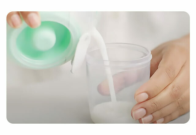 A close up of a woman's hands pouring milk from her Elvie Stride pump into a plastic tumbler