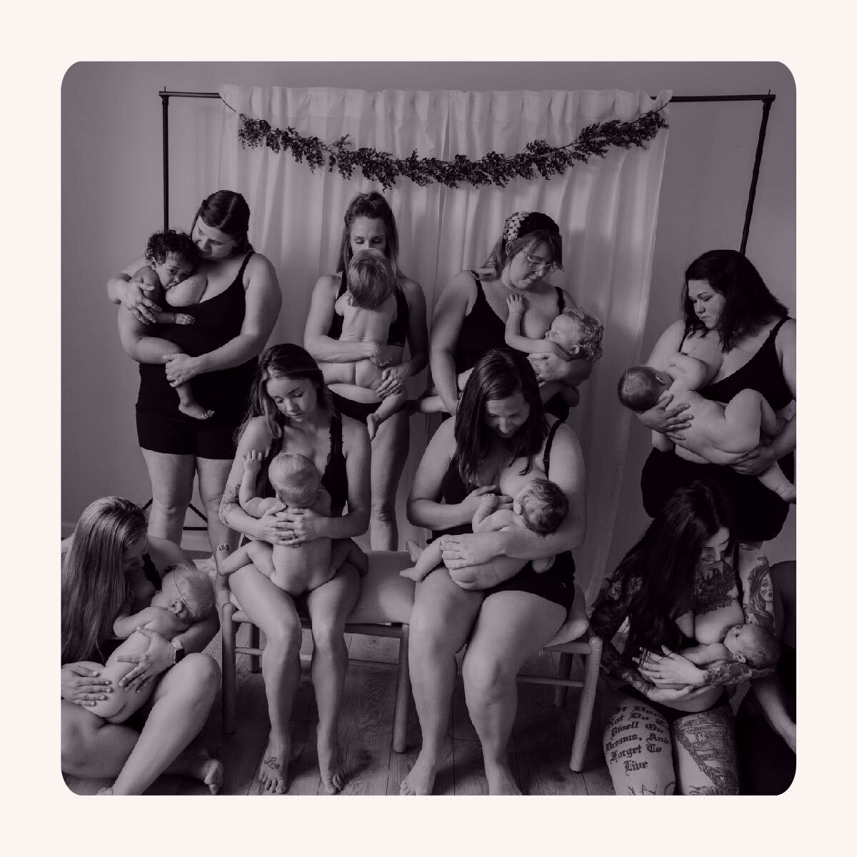 Eight women in their underwear sit on chairs or stand, all breastfeeding their babies. 